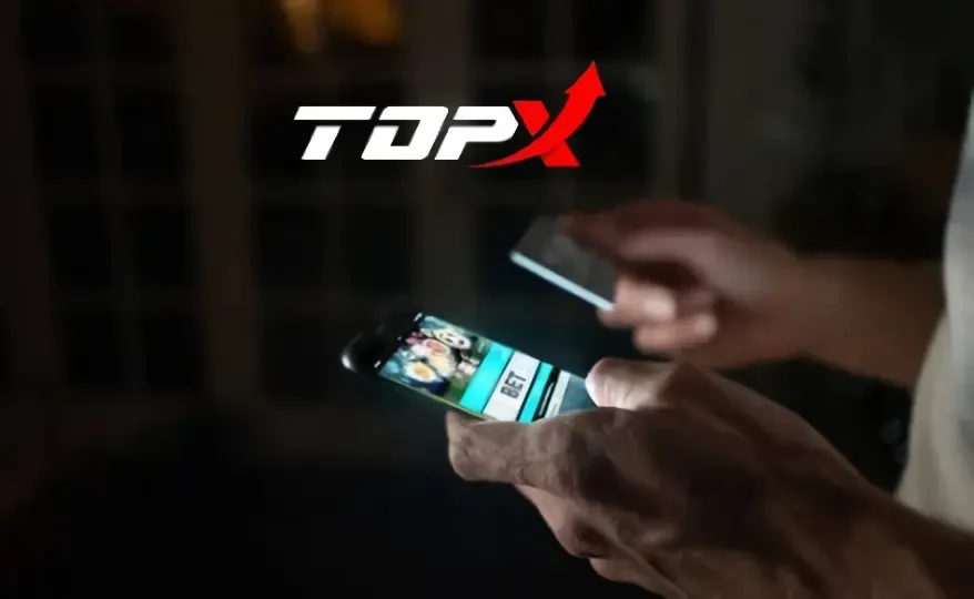 Mãos segurando um celular no escuro, com a marca TopX ao fundo
